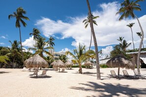 A beach with palm trees, thatched umbrellas, and lounge chairs.