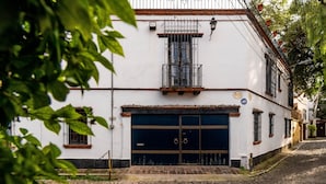 A white building with a dark blue garage door, a small balcony, and a cobblestone street.