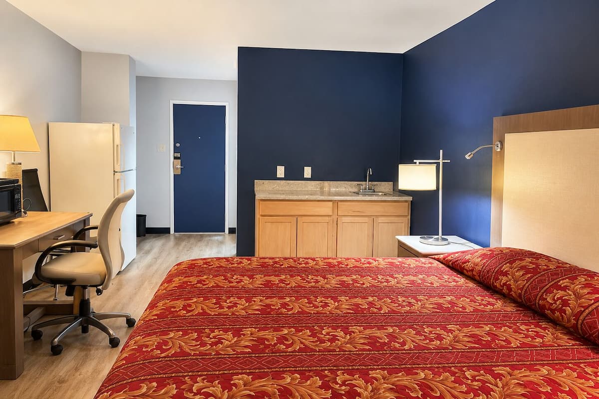 Ein Hotelzimmer mit Bett, Schreibtisch, Stuhl und Küchenzeile.