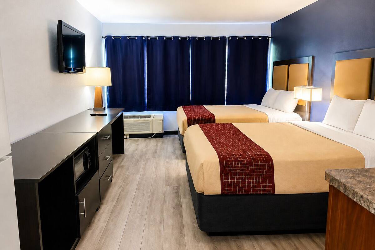 Ein Hotelzimmer mit zwei Betten, einem Schreibtisch, einem Fernseher und einem fensterbepflanzten Fenster.