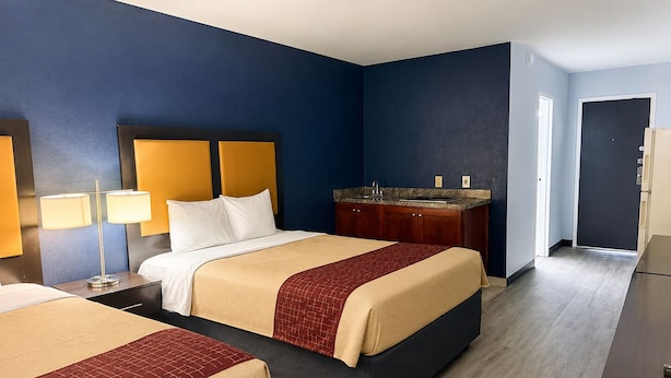 A hotel room with two beds, a nightstand, a desk, a sink, and a door leading to another room. - COUNTRY HOST INN (Franklin)