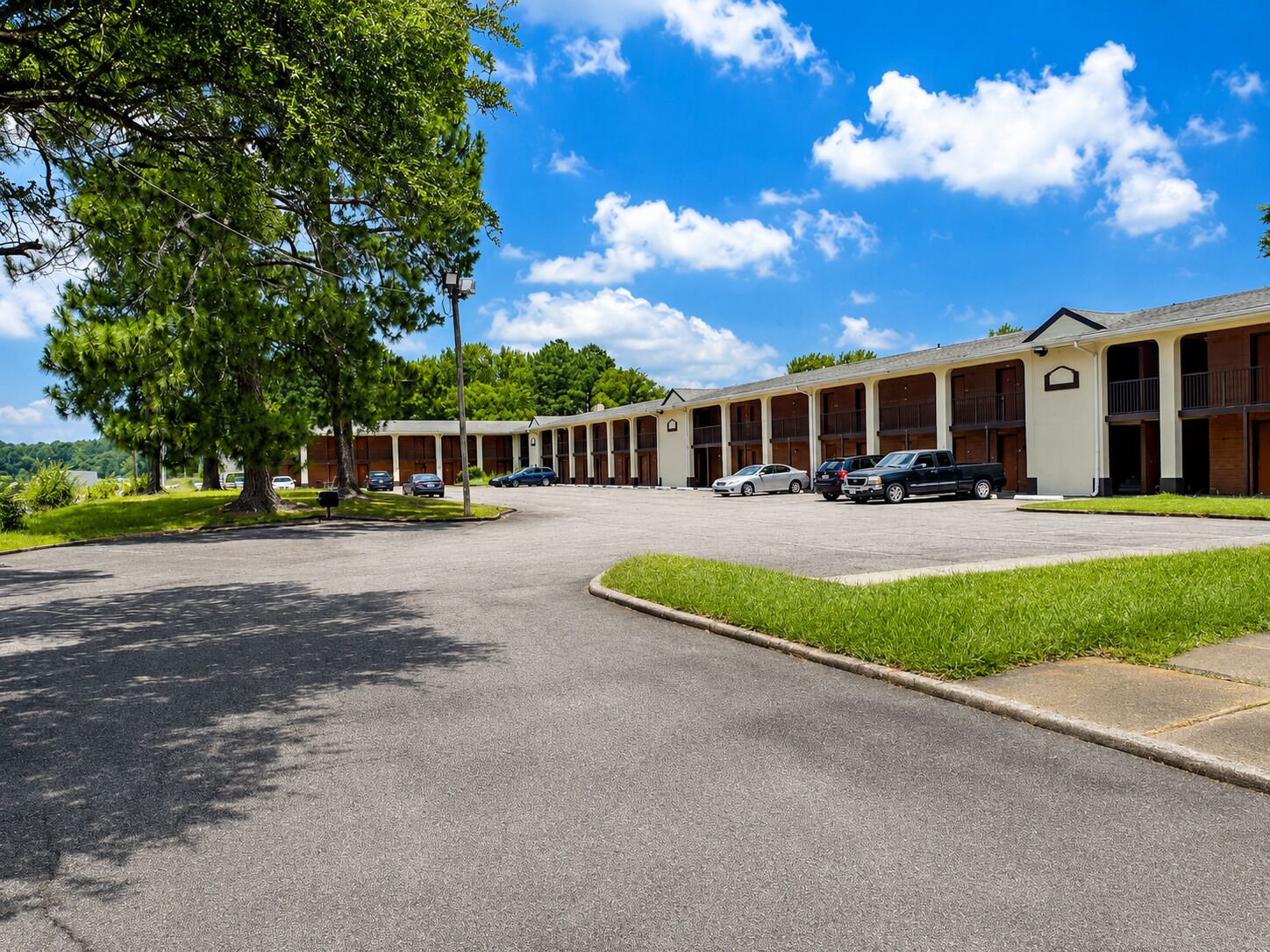 A motel with a central parking area, multiple rooms, and a large tree in the foreground.
