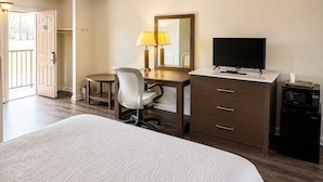 A hotel room with a bed, a desk with a chair, a television, a minibar, and a door leading to a balcony. - COUNTRY HOST INN (Franklin)