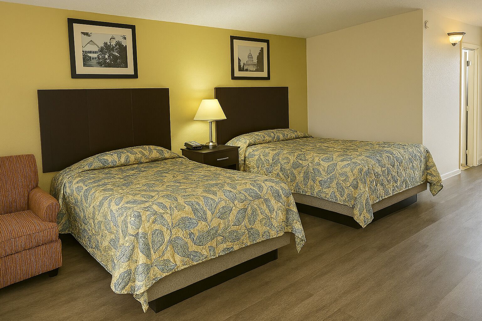 A hotel room with two beds, a nightstand, a lamp, and a chair. There are framed pictures on the wall.