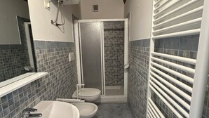 Baño con ducha, dos inodoros, lavabo y espejo.