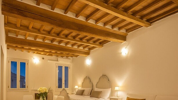 Una habitación amplia con techo de madera, una cama con cabecera, un sofá, una mesa de comedor con sillas y un televisor sobre un mueble.