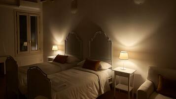 Ein schwach beleuchtetes Schlafzimmer mit zwei Betten, einem Nachttisch mit Lampe, einem Stuhl und einer Holzbalkendecke.