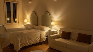 Un dormitorio con cama, mesitas de noche, un sofá y un jarrón con flores.