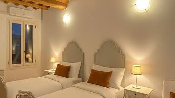 Une chambre d’hôtel avec deux lits, des poutres apparentes en bois au plafond, une fenêtre avec vue et des lampes de chevet.