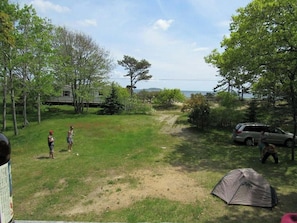 A grassy outdoor area with a tent, a vehicle, and a house in the background.