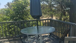 A round table with a metal chair on a wooden deck, an umbrella, and a railing.
