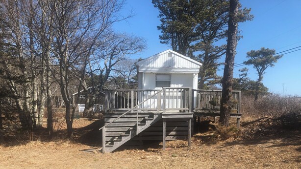 A white cabin with a wooden deck and stairs leading to a front door.