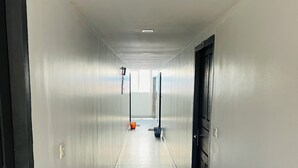 A long, narrow hallway with white walls and a dark floor. There are doors on both sides, and a trash bin is visible in the distance. - Regal Suites (Thiruvananthapuram)