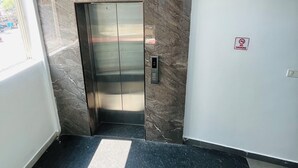 An elevator with a marble wall, a smoke alarm, and a black floor mat. - Regal Suites (Thiruvananthapuram)