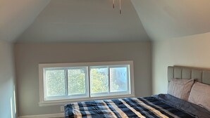 Une chambre avec un plafond en pente, un lit recouvert d’une couvre-lit à rayures et un ventilateur de plafond.
