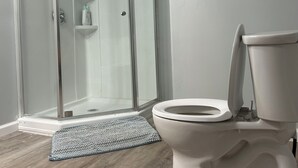 Une salle de bain avec une douche à parois de verre, des toilettes blanches et un plancher en bois.