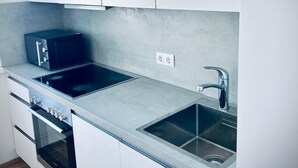 Uma cozinha moderna com armários brancos, micro-ondas preto, pia de aço inoxidável e forno embutido.