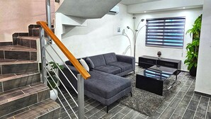 A modern living room with a grey sofa, a coffee table, and a staircase with wooden handrails. - Vane's House 5 minutes from the Consulate (Juárez)