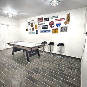 A room with a pool table, three bar stools, and a wall decorated with various automotive and racing memorabilia.