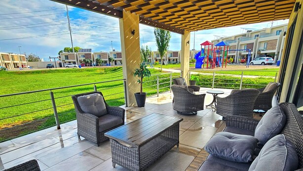 An outdoor patio area with wicker furniture, a wooden table, and a view of a playground and residential buildings. - Vane's House 5 minutes from the Consulate (Juárez)