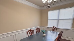 A dining room with a dark wooden table, six chairs, a chandelier, and a window with blinds.