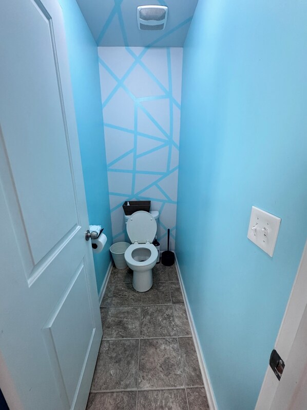 Un baño pequeño con inodoro, un cubo de basura y un calentador fijado a la pared.
