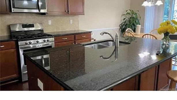 A kitchen with a stainless steel stove, a microwave, and a granite countertop.