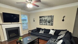 A living room with a dark gray sofa, a black coffee table, a flat-screen TV, a fireplace, and a ceiling fan.