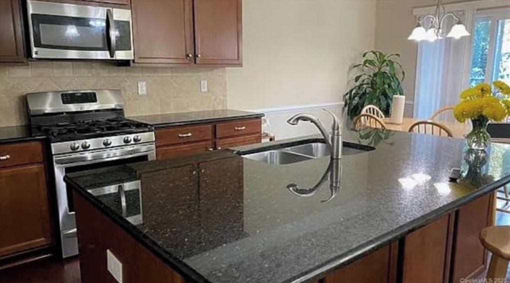 Una cocina con estufa de acero inoxidable, microondas y encimera de granito.