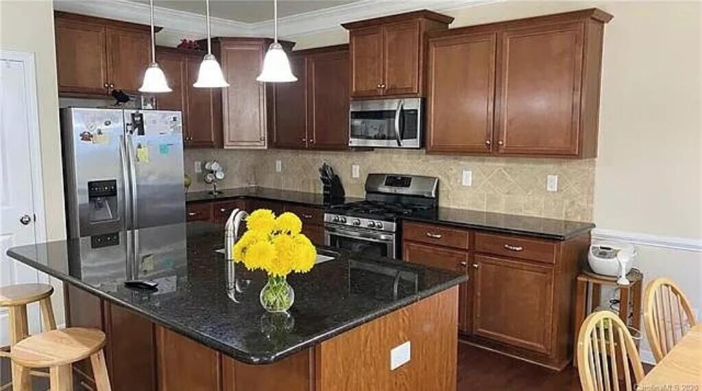 A kitchen with wooden cabinets, stainless steel appliances, a granite countertop, and a vase with yellow flowers.