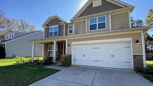 A two-story house with a garage, a covered porch, and a well-maintained lawn.
