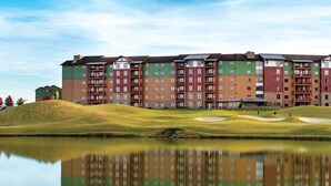Ein mehrstöckiges Hotel mit einem spiegelnden Pool davor, umgeben von grünen Hügeln und blauem Himmel.