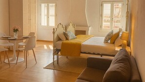 Una habitación amplia con techo de madera, una cama con manta amarilla, un sofá y una zona de comedor con sillas y una mesa.