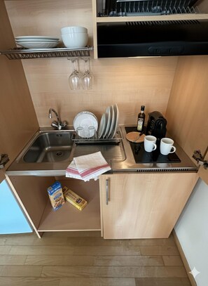 Une cuisine de taille réduite, équipée d’un évier, d’un égouttoir et de placards de rangement.