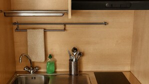 Una cocina compacta con lavamanos, grifo de acero inoxidable, una pequeña encimera y una estufa negra.