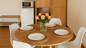 Un comedor con una mesa redonda de madera, sillas blancas y un jarrón de flores.