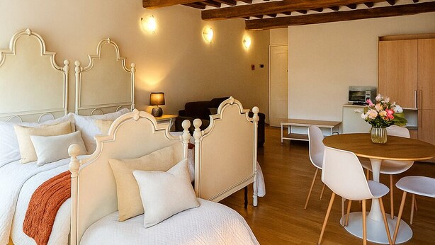 Un dormitorio con una cama grande, techo de madera, zona de comedor con mesa y sillas, y una cocina al fondo.