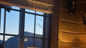 A cozy room with a large window, wooden walls, and a lamp on a wooden table.