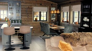 A cozy log cabin interior with a dining area, bar stools, and a sofa with a fur throw.