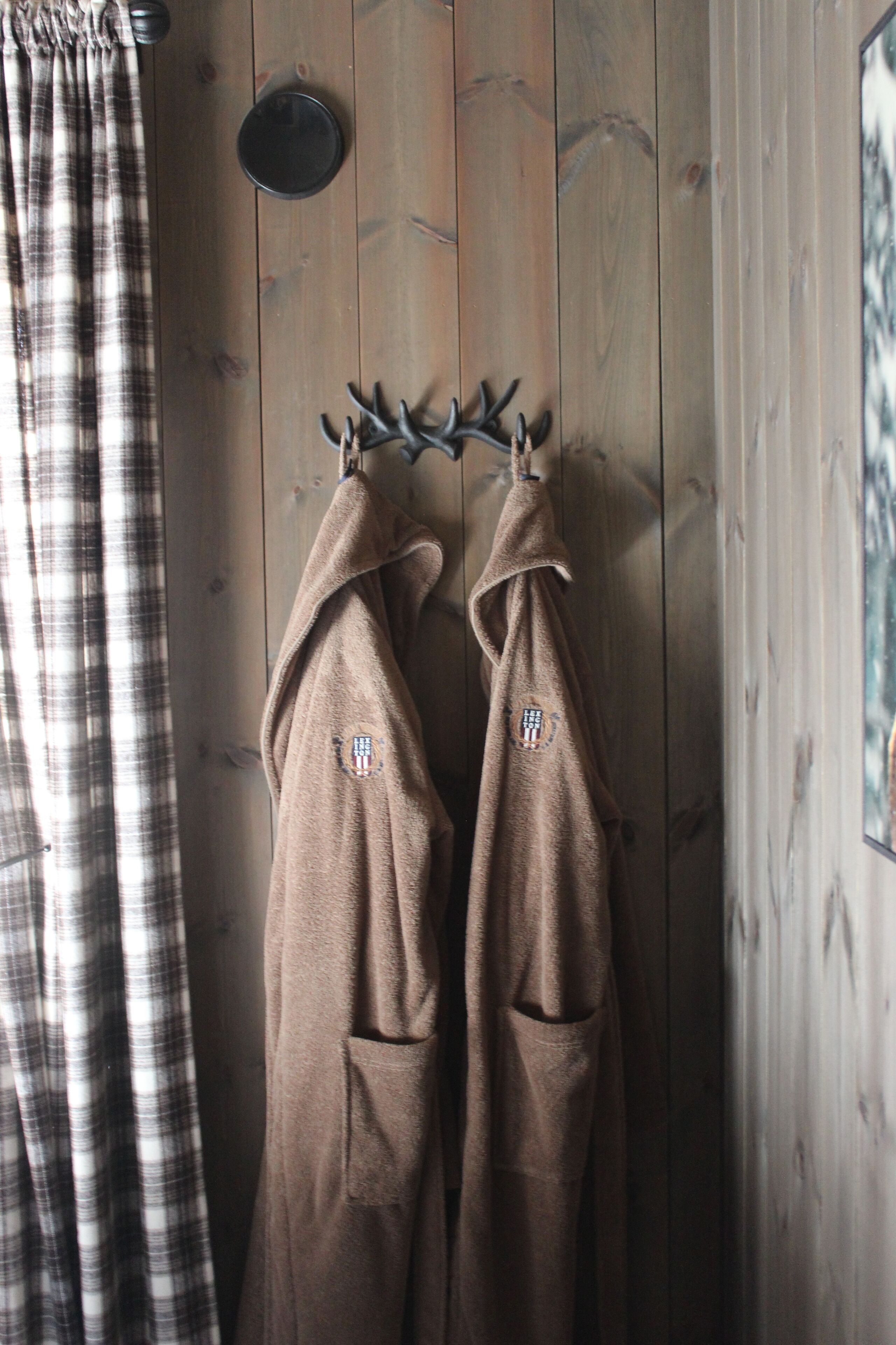 A wooden wall with a coat rack holding two brown jackets with a logo.