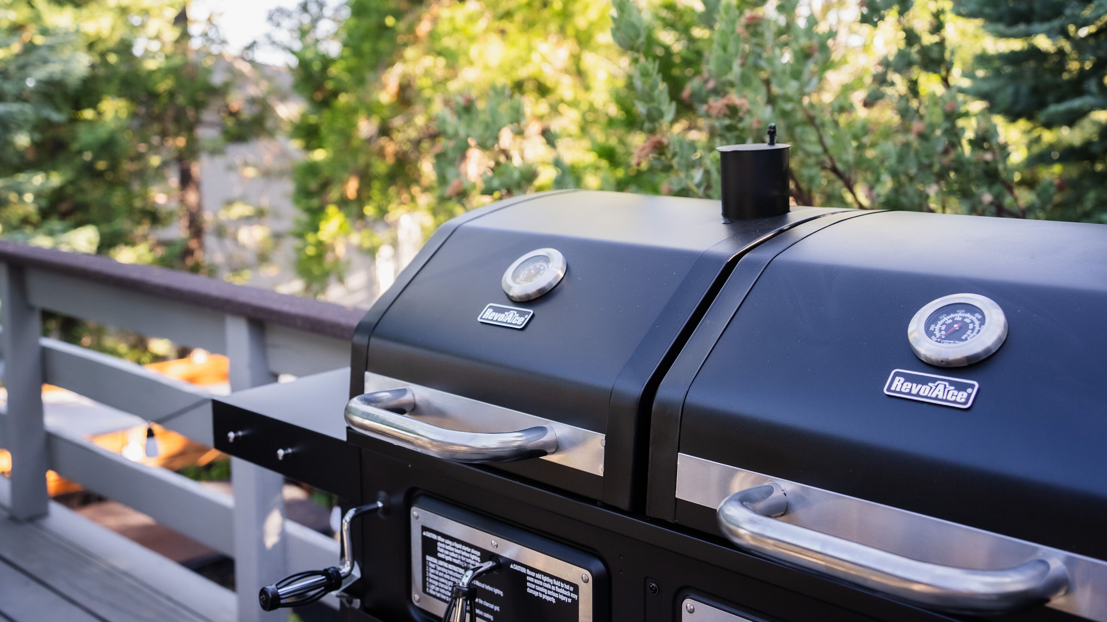 A charcoal grill with two control knobs and a digital display, mounted on a wooden deck with a railing.