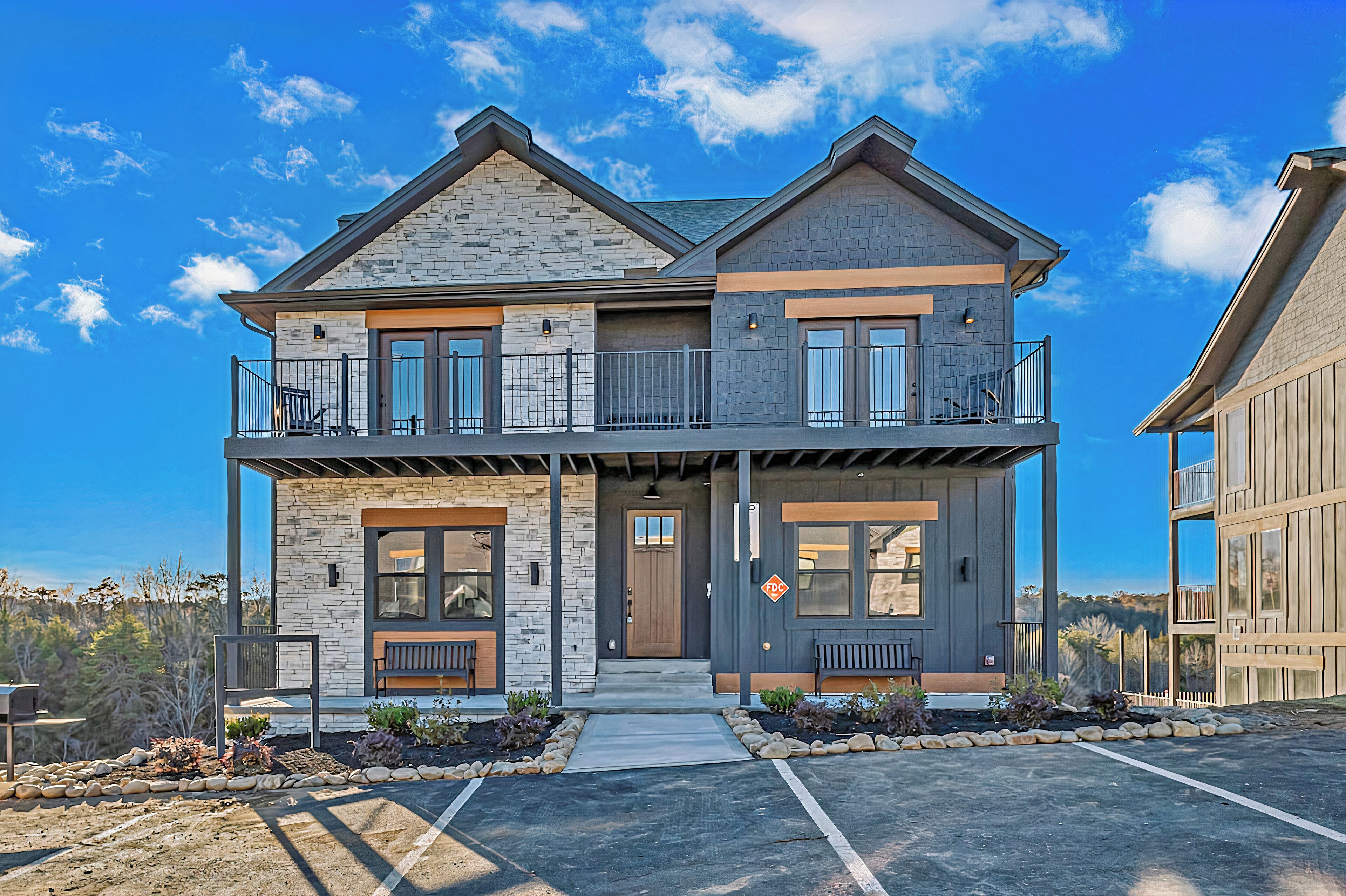 A two-story house with a stone facade, a balcony on the upper floor, and a front porch with seating.