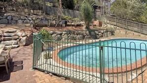 A swimming pool surrounded by a stone wall and a wooden fence, with trees and a clear sky in the background. - Spacious Family Retreat with Pool/Pet friendly (Kenmore)