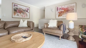 A modern living room with a brown leather sofa, a smaller armchair, a round coffee table with a remote control, and a lamp on a pedestal. - Spacious Family Retreat with Pool/Pet friendly (Kenmore)