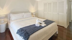A neatly made bed with white linens and a gray throw blanket, a bedside lamp, and a white nightstand. - Spacious Family Retreat with Pool/Pet friendly (Kenmore)