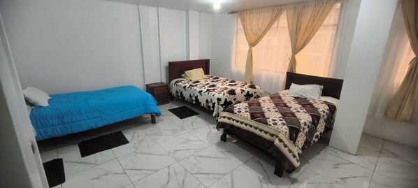 A bedroom with two beds, a nightstand, and a window with curtains. - Hostal y Complejo Turistico La Rueda (Guaranda)