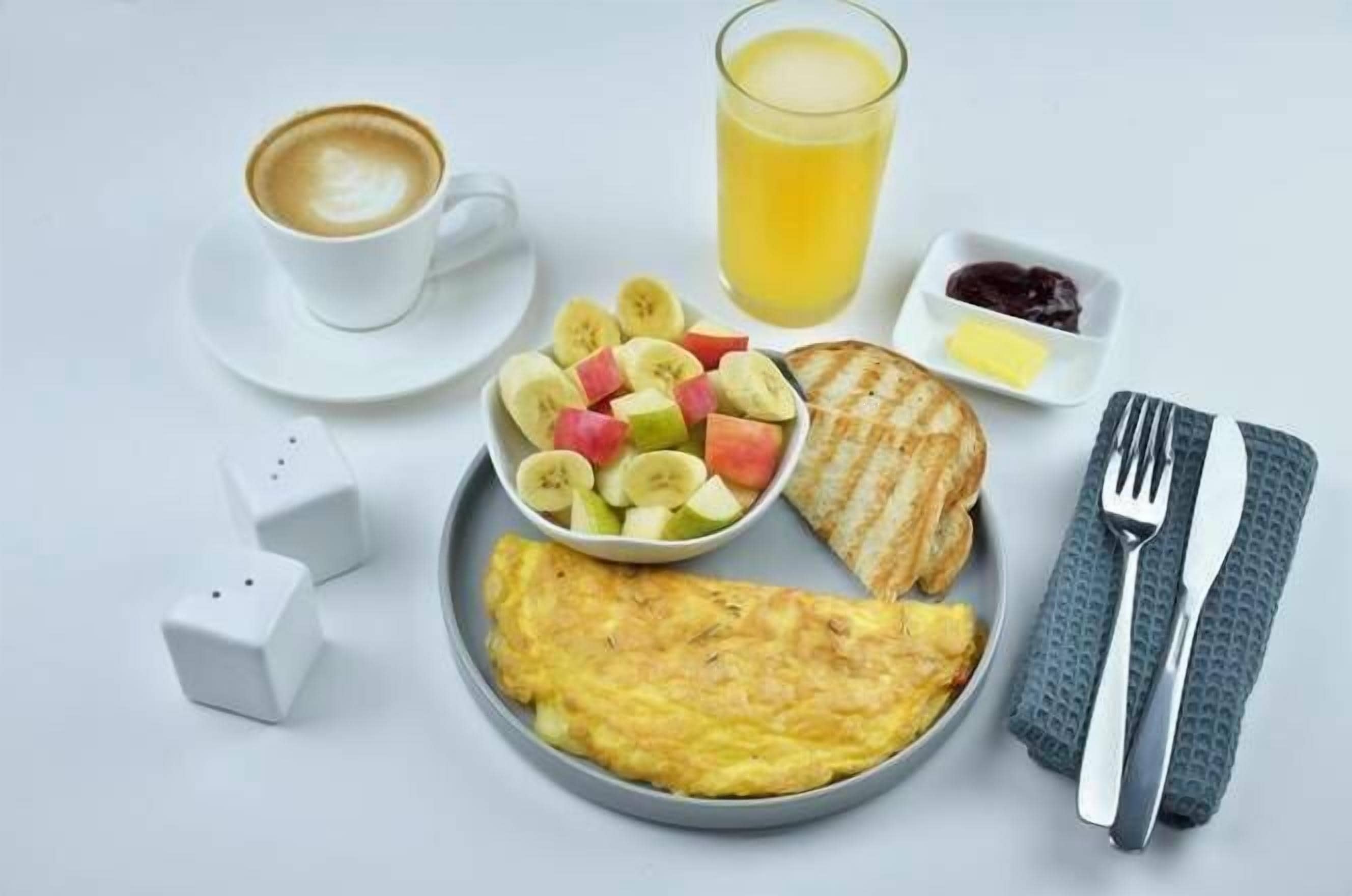 A breakfast plate with an omelette, toast, fruit, and a glass of orange juice.