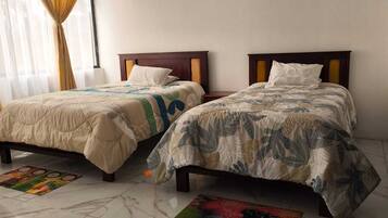 Two beds with headboards, a window with curtains, and a patterned rug on the floor.