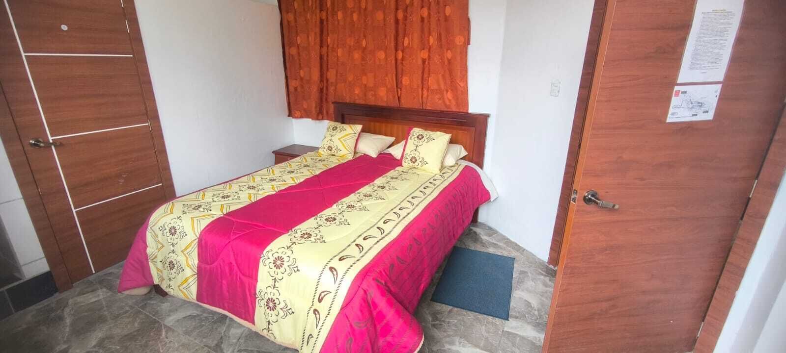 A single bed with a patterned bedspread, a wooden headboard, and a wooden wardrobe.