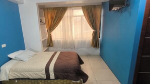 A bedroom with a bed, a window with curtains, and a blue wall. - Hostal y Complejo Turistico La Rueda (Guaranda)